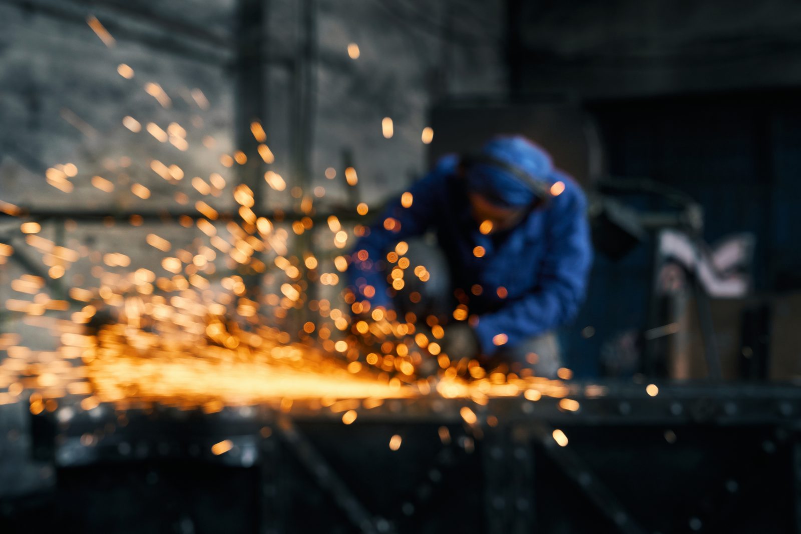 Worker grinding steel with sparks flying in a fabrication shop